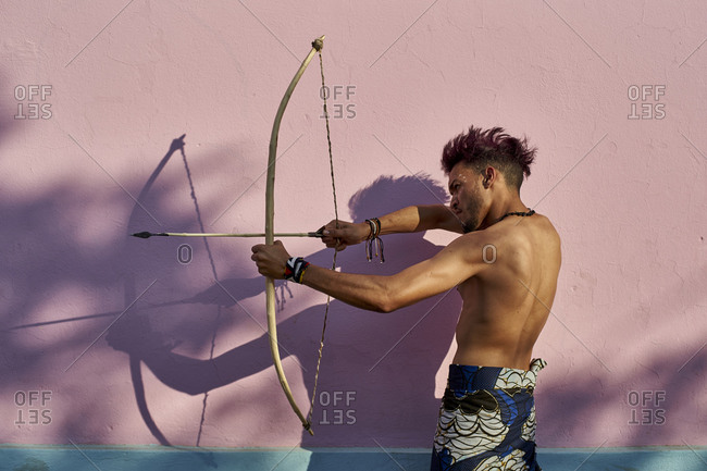 Barechested young man with bow and arrow outdoors