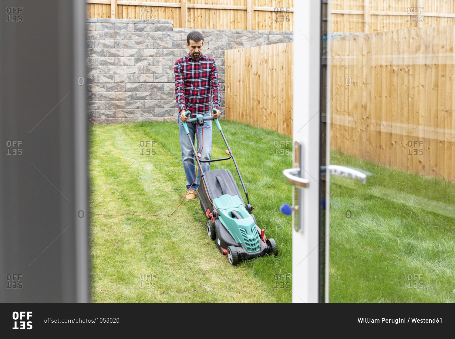 Man mowing lawn with push lawn mower at backyard
