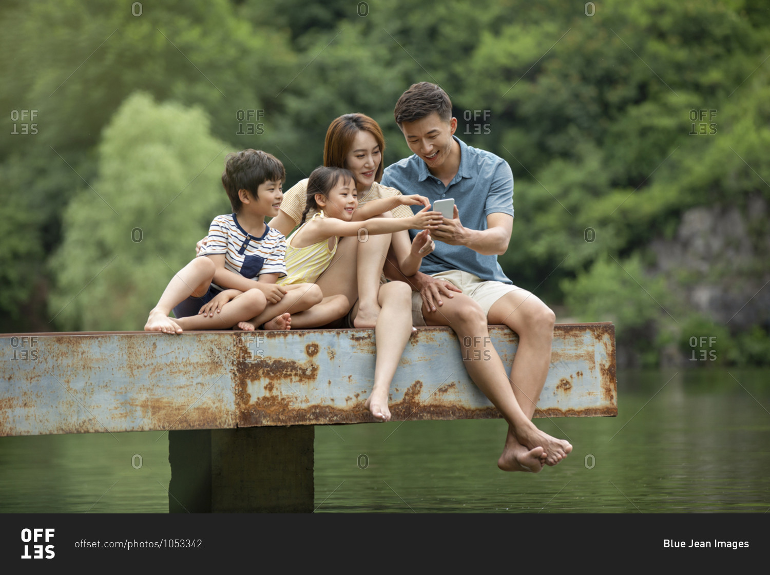 Happy young Chinese family using smartphone at jetty
