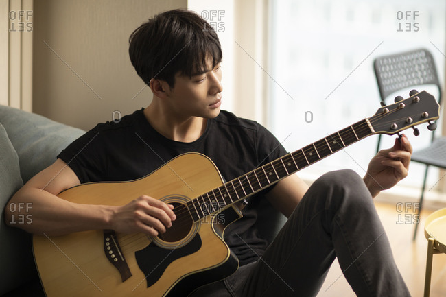 Young Chinese man playing guitar at home