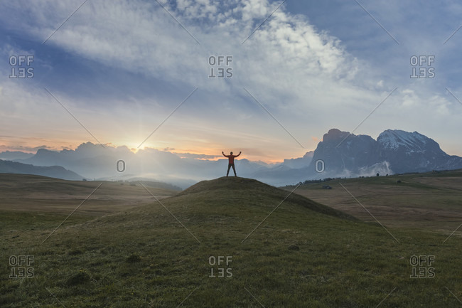 Hiker standing in silhouette at dawn on the meadows of the alpe di siusi, in the background the sassolungo / langkofel, dolomites, kastelruth, south tyrol, italy
