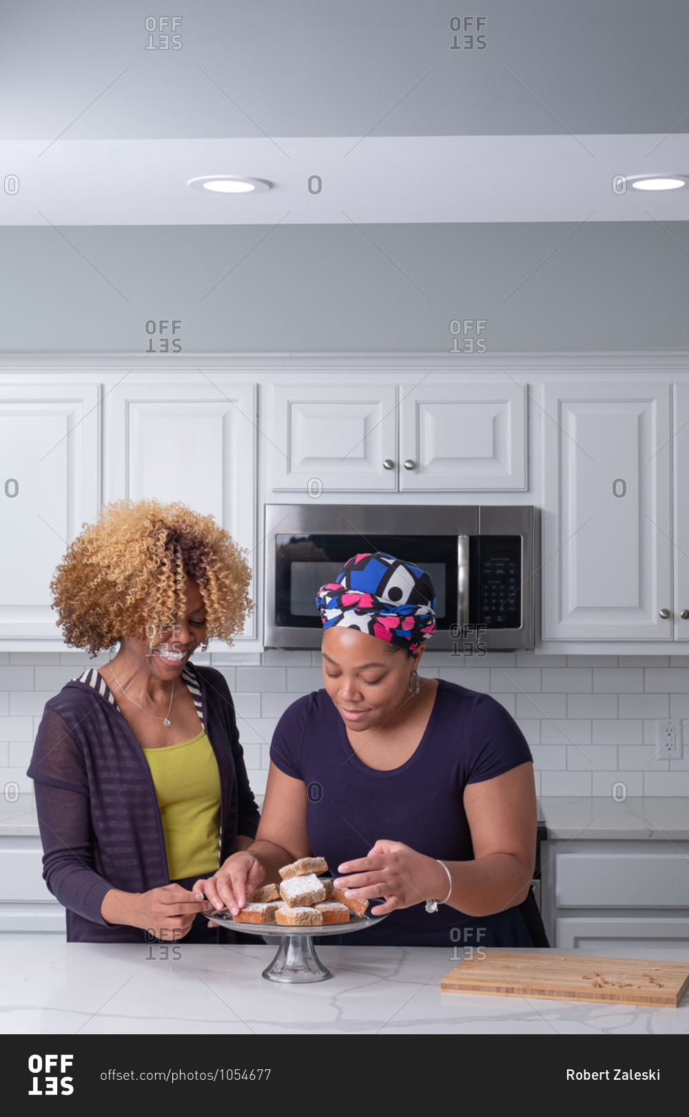 African American mother and daughter arranging fresh baked brownies on a glass stand in kitchen