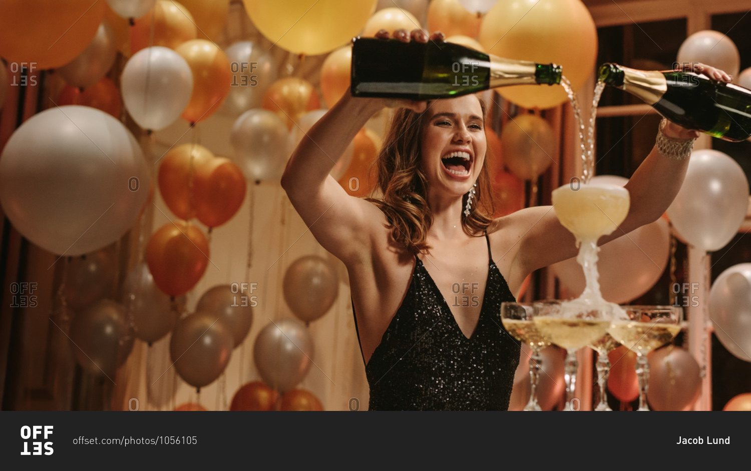 Excited young woman filling champagne into a tower glasses at gala night party. Beautiful female socialite enjoying at new years party.
