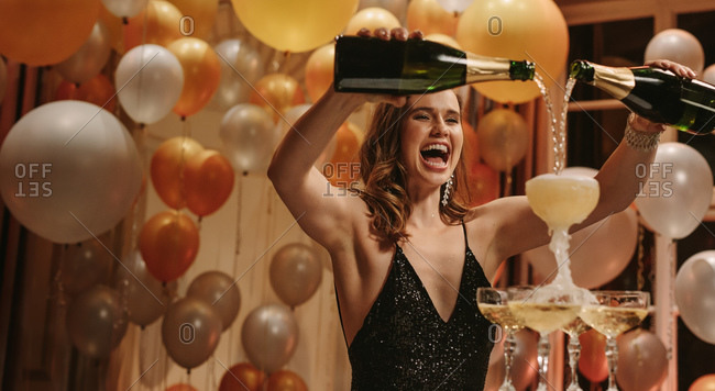 Excited young woman filling champagne into a tower glasses at gala night party. Beautiful female socialite enjoying at new years party.