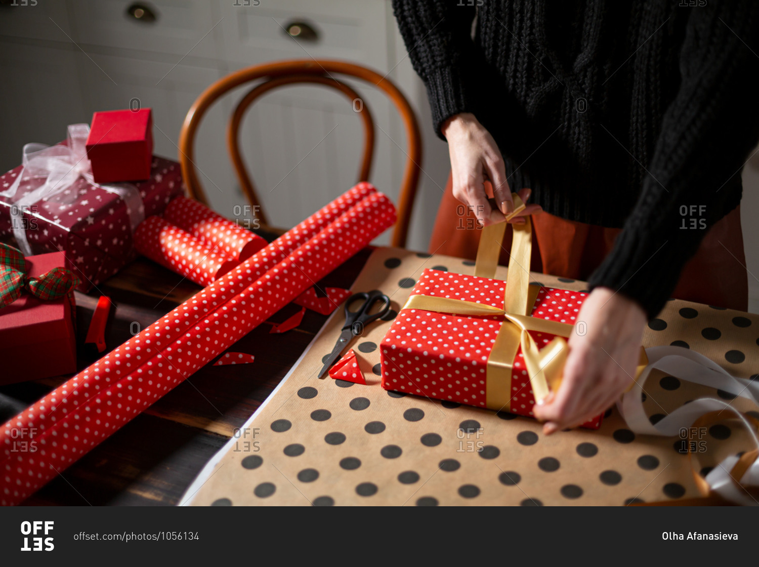 Person wrapping Christmas gifts with golden ribbon
