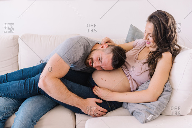 Young couple looking happy and in love expecting their child while man listens to wife's belly