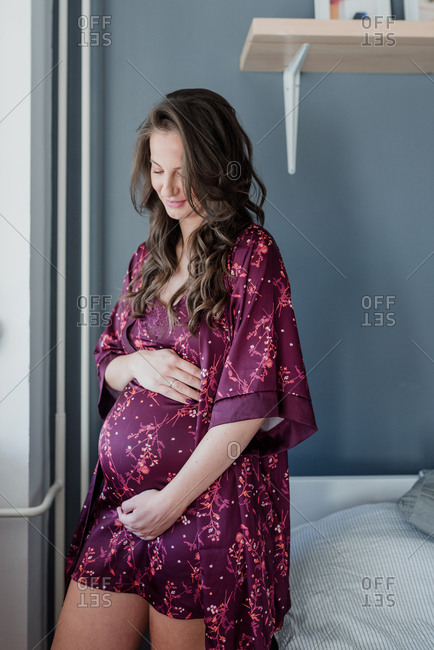 Beautiful pregnant woman holding her belly wearing a silky night gown