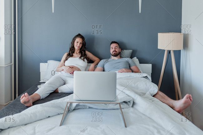 Young couple with the baby on the way relaxing in the bedroom watching a movie