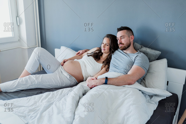 Happy young couple with the baby on the way relaxing in the bedroom watching a movie