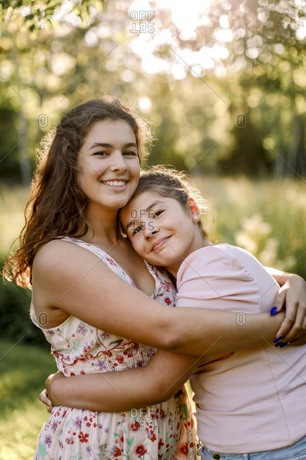 Portrait of smiling teenager embracing sibling in backyard