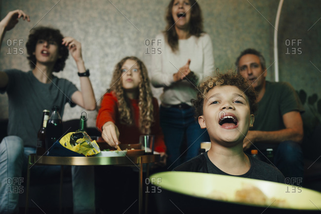 Boy shouting while family cheering during sporting event at night
