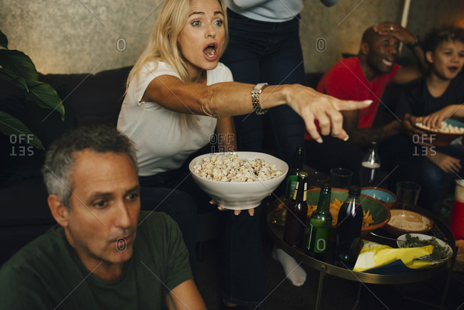 Woman with mouth open gesturing by family while eating popcorn during sporting event
