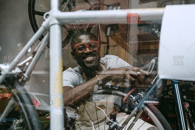 Portrait of smiling owner repairing bicycle in workshop seen through glass window