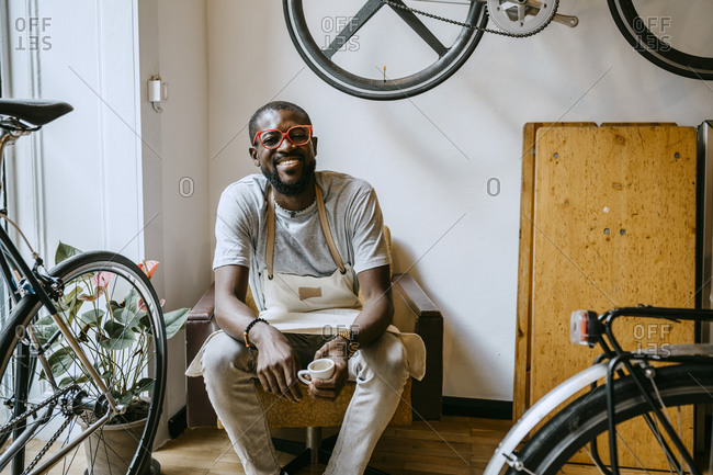 Portrait of male owner with coffee cup sitting in bicycle shop