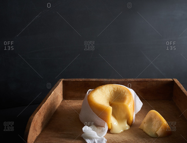 A cheese with a ripe, melting middle with a slice cut out on a wooden board