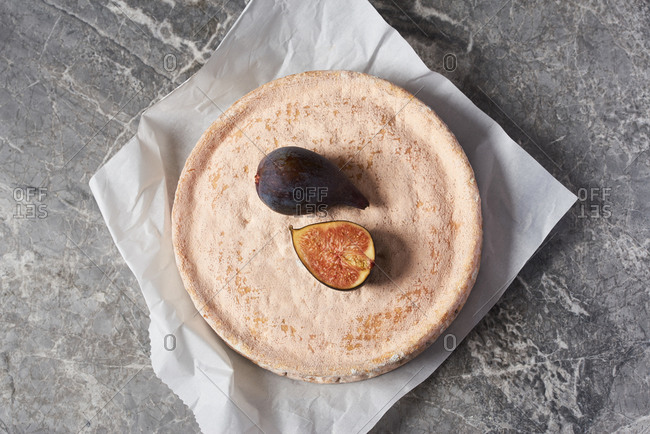 A large wheel of specialty cheese with a pink rind, served with figs on a marble board