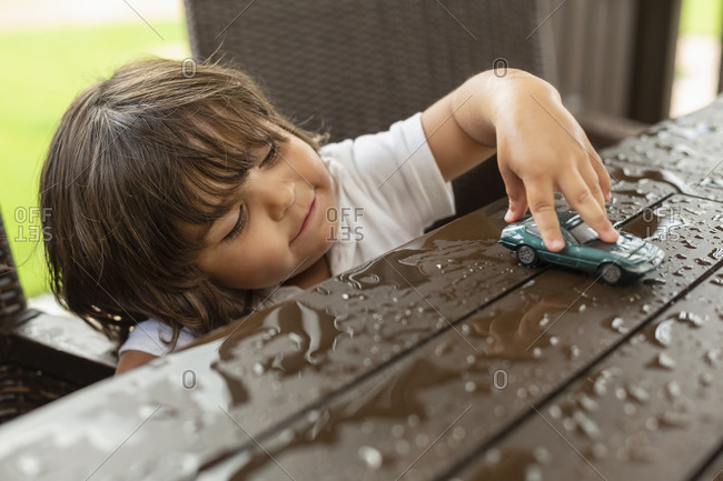 Cute toddler boy playing with toy car on wet patio table