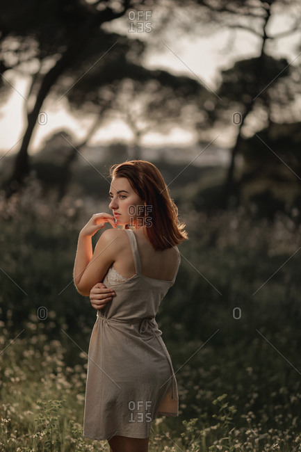 Peaceful female wearing summer dress standing on lawn in park in iceland and tenderly looking away