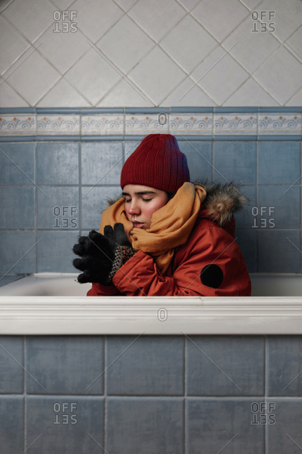 Young female with closed eyes in knitted hat and gloves sitting in bath at home