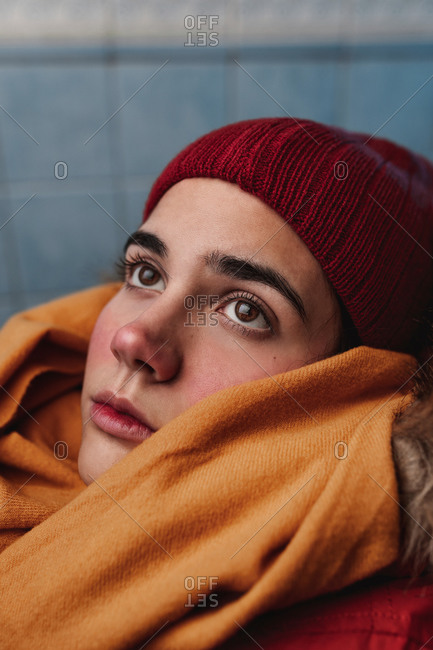 Young contemplative ethnic female in trendy knitted hat and scarf looking away on blurred background