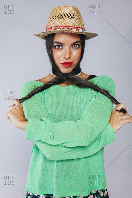 Confident young long haired brunette with red lips wearing colorful clothes and trendy straw hat