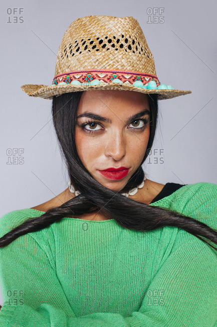 Confident young long haired brunette with red lips wearing colorful clothes and trendy straw hat