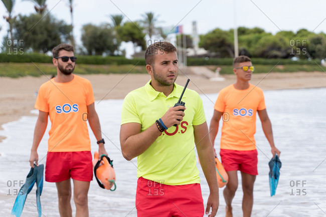 Male employees in bright wear with walkie talkie radio and flippers standing on wavy sea while looking away