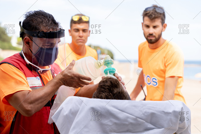 Male lifeguards carrying stretcher with patient in oxygen mask on ocean shore in summer