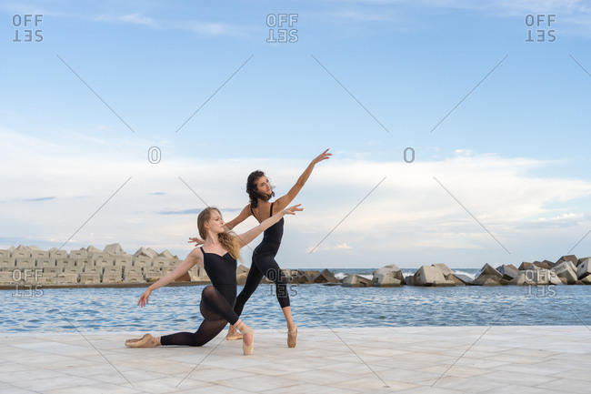 Full length of creative young female dancers in black clothing performing various dance movements on waterfront near sea