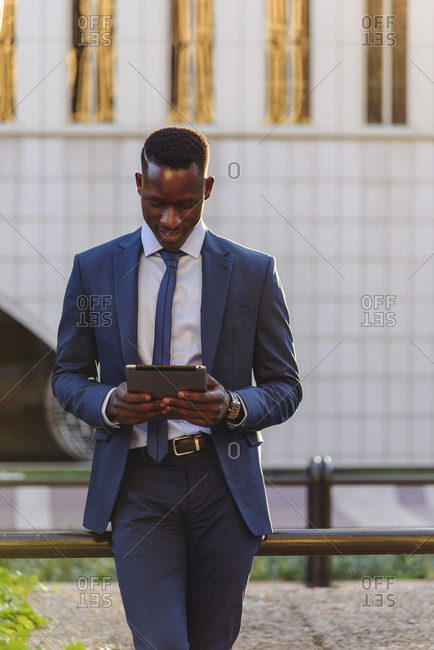 Full body side view of confident respectable african american businessman in formal outfit leaning on street against contemporary buildings in modern downtown
