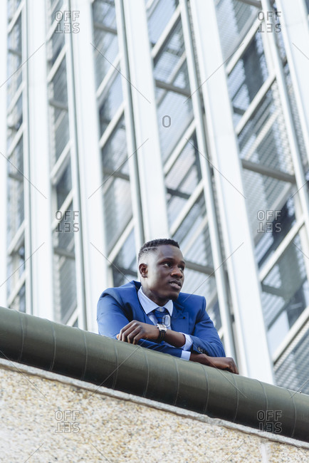 Low angle of confident respectable african american businessman in formal outfit leaning on street against contemporary buildings in modern downtown