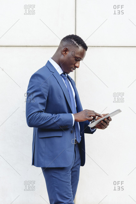 Confident respectable african american businessman in formal outfit leaning on street against contemporary wall in modern downtown with smartphone