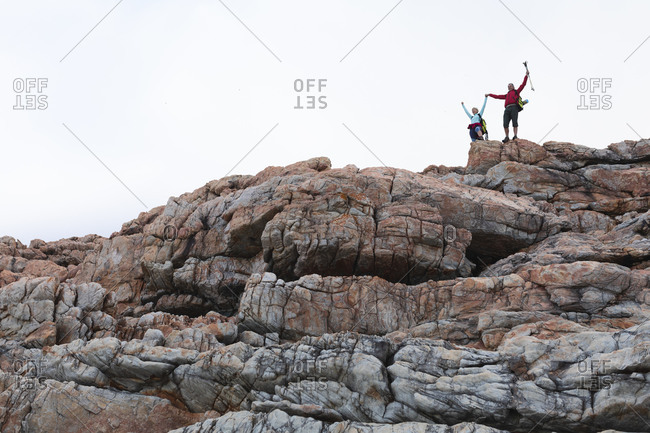 Senior couple spending time in nature together, walking in the mountains, holding hands, raising arms up.