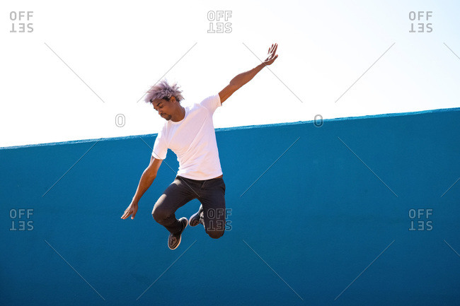 Black and afro man dressed in white jumping on a blue wall. parkour concept.