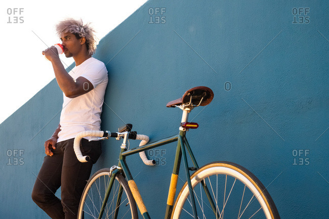 Black man and afro biker drinking takeaway coffee on a blue wall. black biker concept. take away coffee.