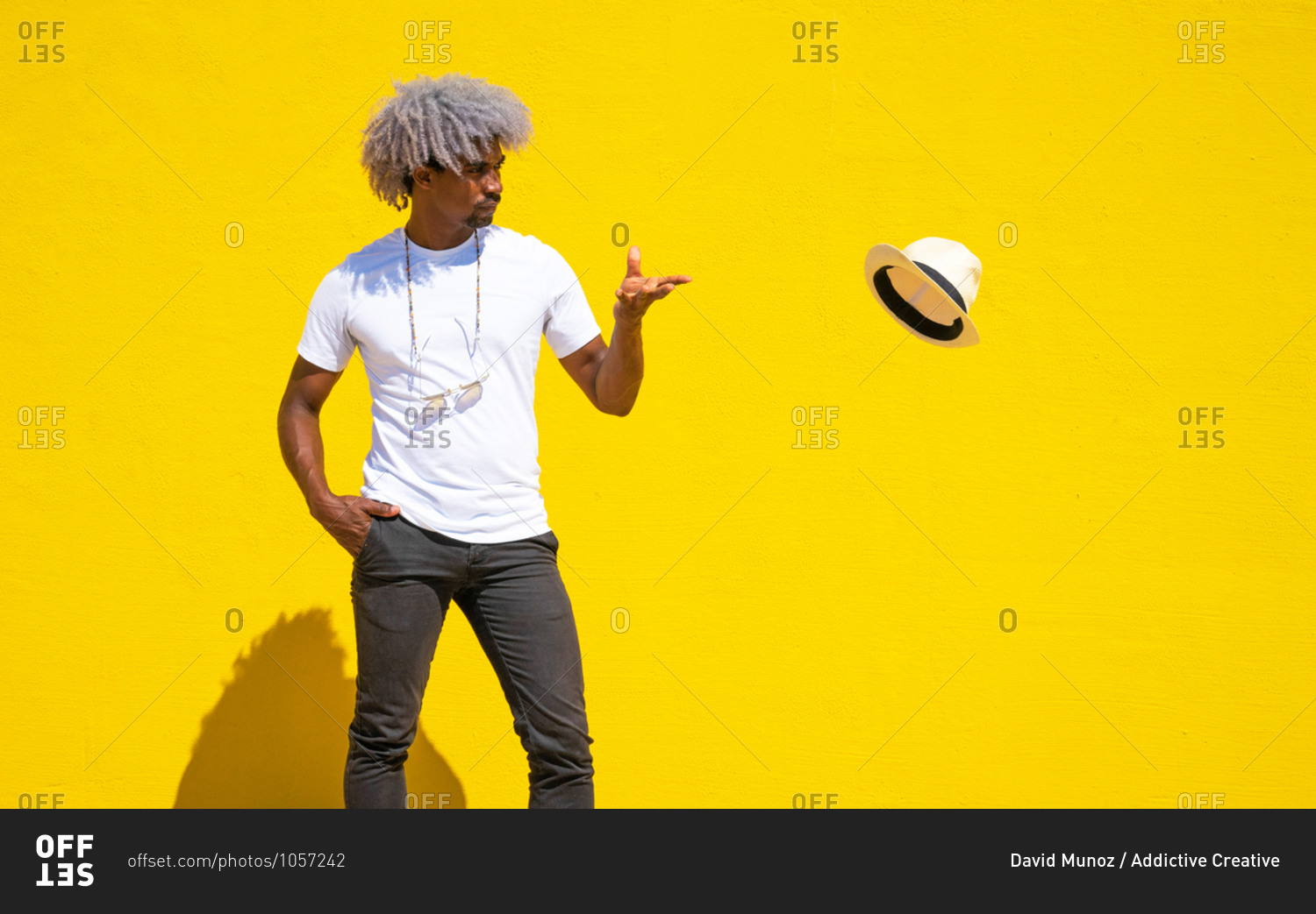 Black man with afro hair throwing a straw hat on a yellow background. concept of throwing a hat.