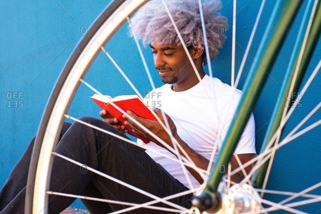 Black and afro man reading a book next to his bicycle. concept of black man reading a book.