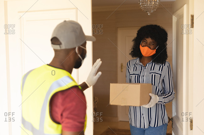 Delivery man wearing face mask delivering package to woman wearing face mask at home.
