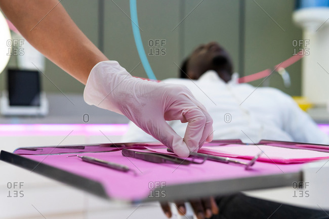 Unrecognizable doctor in latex gloves standing near table with various dental tools while preparing for treatment in medical room