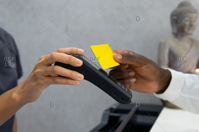 Cropped unrecognizable african american female manager in medical mask receiving payment via pos terminal and plastic card from crop male patient in modern clinic