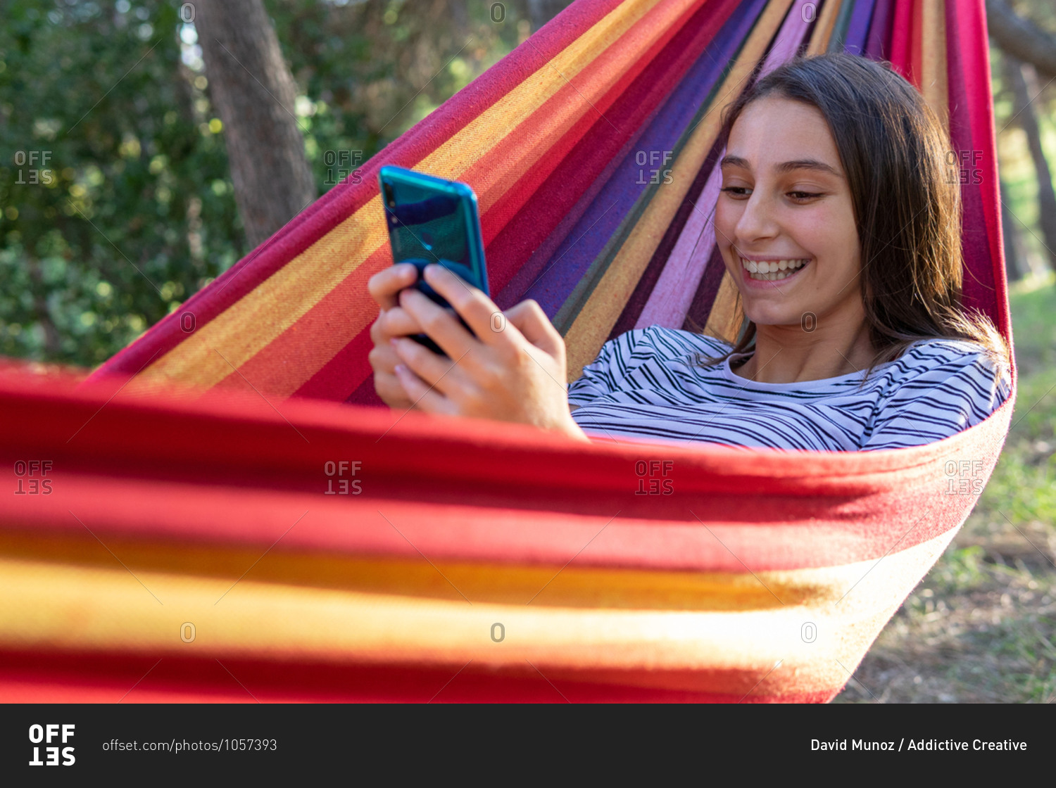 Resting woman lying in hammock and watching movie on mobile phone while spending weekend in park in summer on sunny day