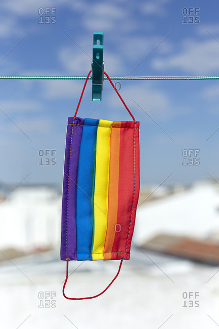 Protective mask with picture of lgbt rainbow flag attached with clothespin to thread on sunny day in backyard