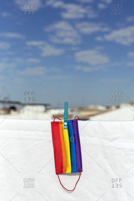 Protective mask with picture of lgbt rainbow flag attached with clothespin to thread on sunny day in backyard on background of white bed sheet