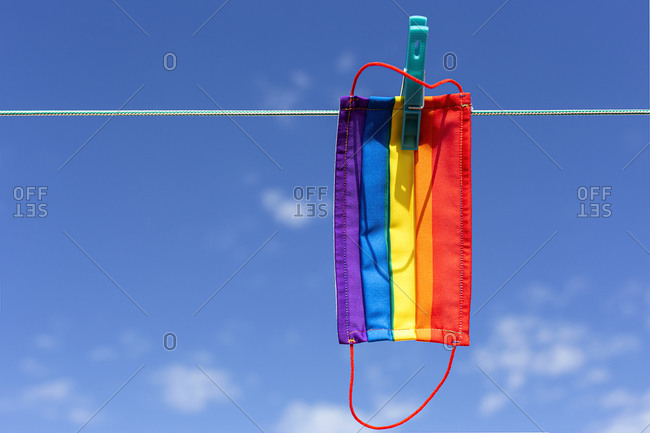 Protective mask with picture of lgbt rainbow flag attached with clothespin to thread on sunny day in backyard