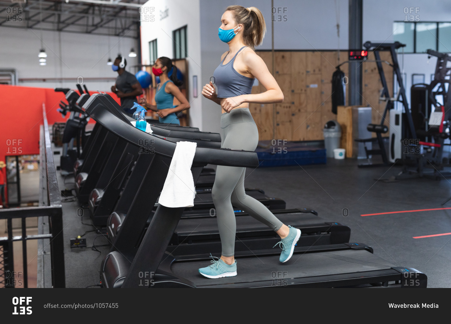 Fit caucasian woman wearing face mask running on treadmill doing cardio workout in the gym.