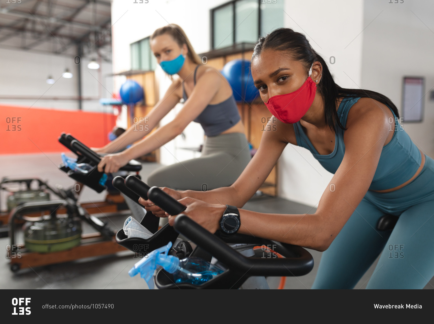 Portrait of two fit caucasian woman wearing face masks exercising on stationary bike in the gym.