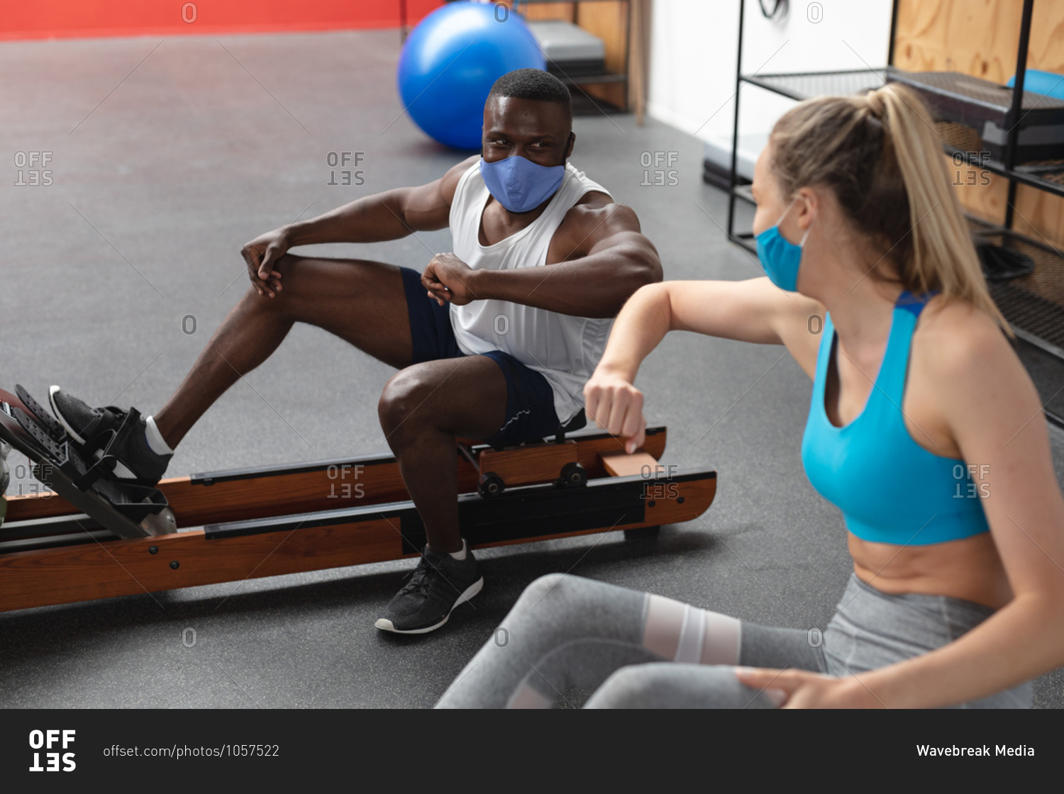 Fit African American man and Fit caucasian woman wearing face masks greeting each other by touching elbows while exercising in the gym.