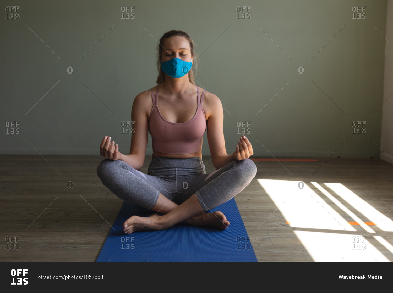 Fit caucasian woman wearing face mask practicing yoga while sitting on yoga mat in the gym.