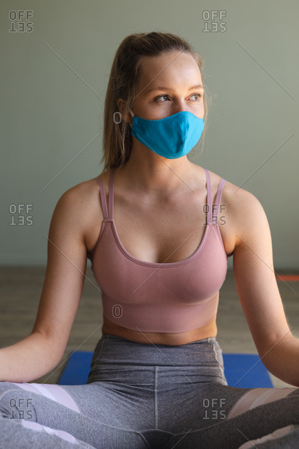 Mid section of Fit caucasian woman wearing face mask practicing yoga in the gym.