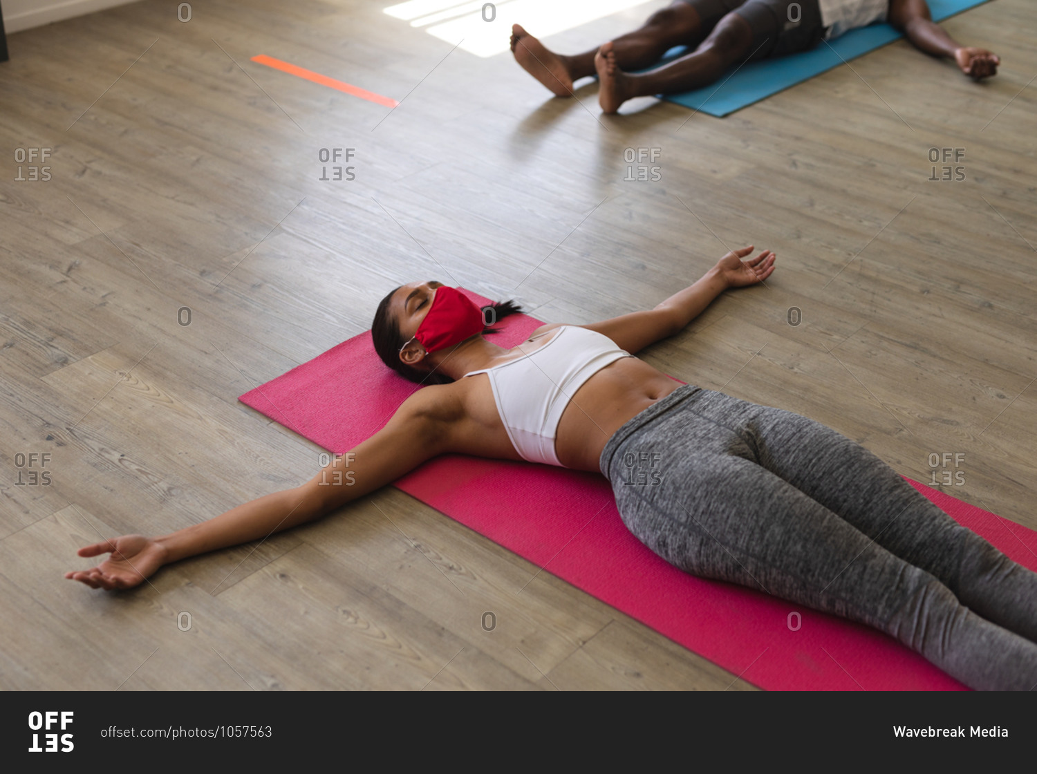 Fit woman caucasian wearing face mask practicing yoga while lying on yoga mats in the gym.
